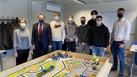 Kultusminister Lorz gemeinsam mit Schülerinnen und Schüler der First Lego League Challenge. Sie stehen um einen Tisch herum wo die Roboter getestet werden. 