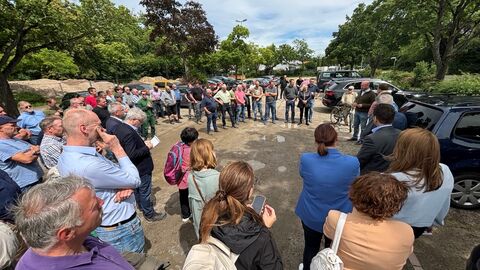 Eine größere Ansammlung Menschen steht auf einem Parkplatz versammelt und sieht dem Landwirtschaftsminister zu, der ebenfalls dort steht und spricht.