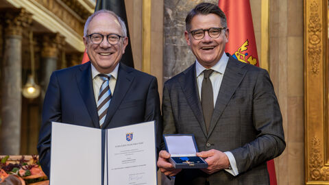 Zwei Personen stehen nebeneinander und halten die Auszeichnung hoch.