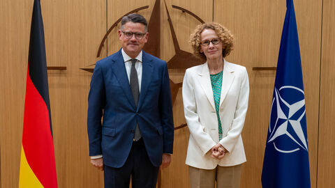 Ministerpräsident Boris Rhein (links), der neben der Flagge der Bundesrepublik Deutschland steht, trifft NATO-Generalsekretärin Radmila Šekerinska (rechts), die neben der Flagge der NATO steht.