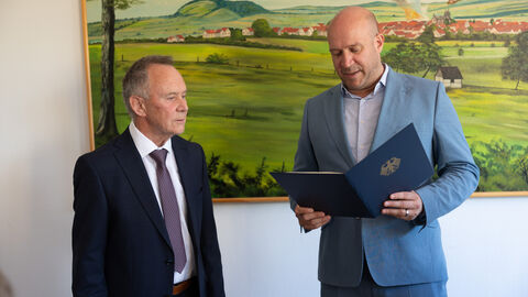 Zwei Männer stehen nebeneinander in einem Raum. Staatsminister Jung hält eine Urkunde in der Hand.