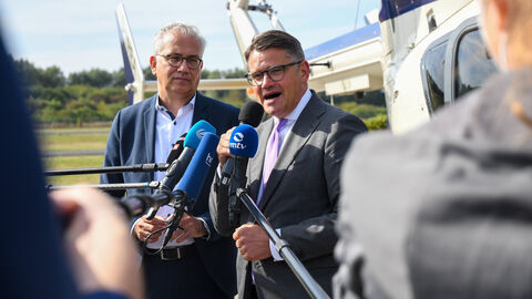 Ministerpräsident Rhein, vom Betrachter aus rechts, und Wirtschaftsminister Al-Wazir, vom Betrachter aus links, stehen auf dem Flugplatz in Egelsbach vor einem Löschhubschrauber und sprechen in ihnen entgegengestreckte Mikrofone.