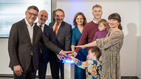 Sechs Erwachsende und zwei Kinder stehen in einem Halbkreis und strecken jeweils einen Arm in die Mitte.