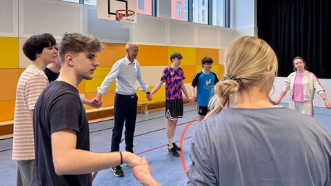 Minister Schwarz und Schüler und Schülerinnen stehen in einer Turnhalle im Kreis und halten sich an den Händen